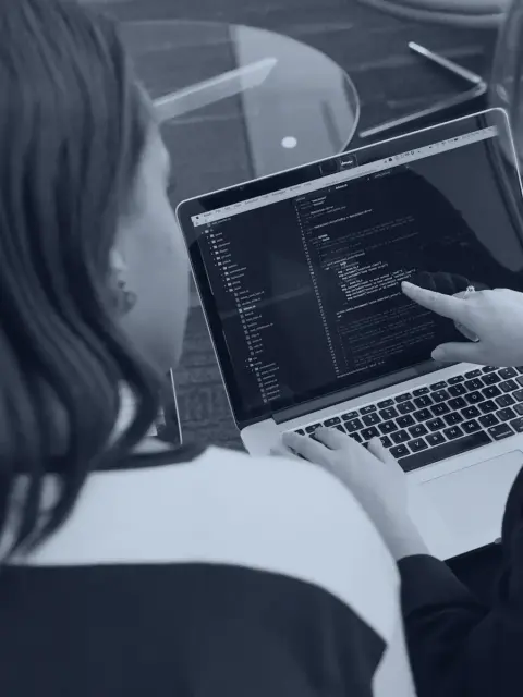 One colleague pointing out a line of code on a laptop while another types